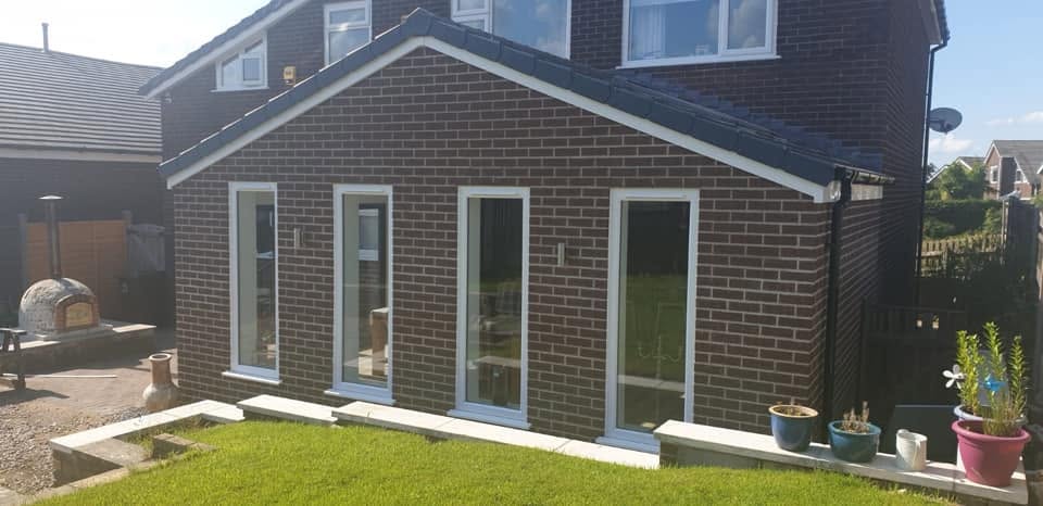 Completed single-storey brick house extension with pitched roof and glazed doors overlooking the garden